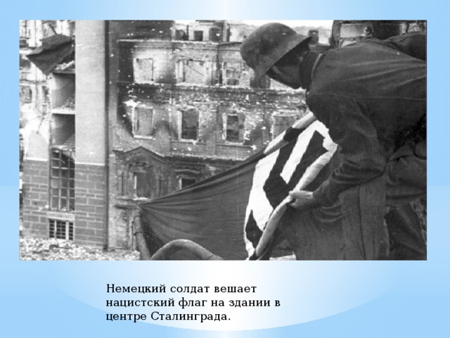 Немецкий солдат вешает нацистский флаг на здании в центре Сталинграда. 