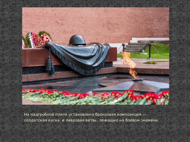 На надгробной плите установлена бронзовая композиция —  солдатская каска   и лавровая ветвь, лежащие на боевом знамени. 